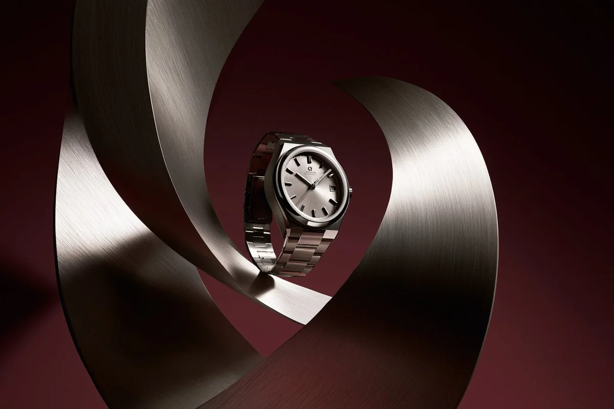 A premium studio product photo of a wristwatch centered inside looping brushed-metal sculptural forms on a deep burgundy background.